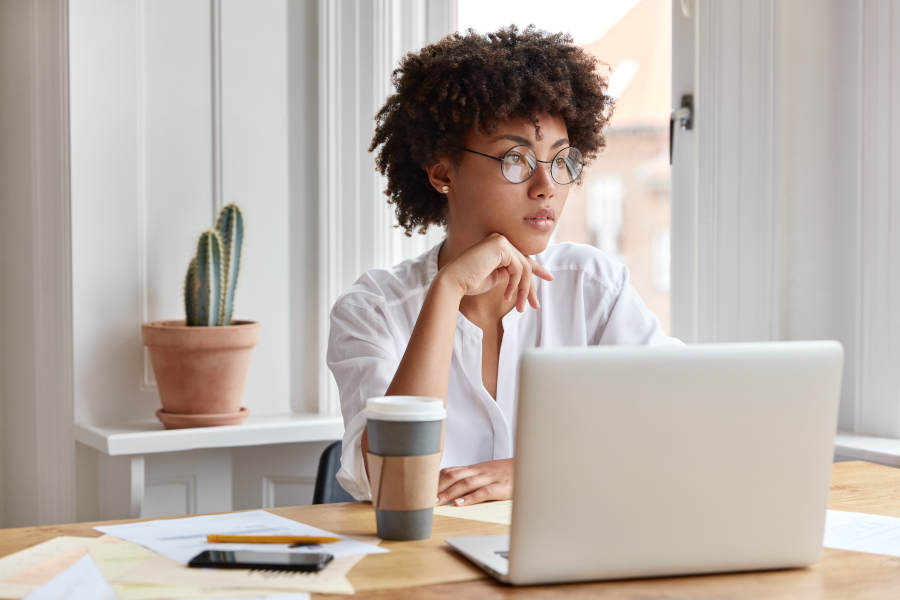 Paperwork concept. Experienced thoughtful African American administrative manager works with financial documents and modern electonic gadgets, wears round spectacles, poses against cozy interior