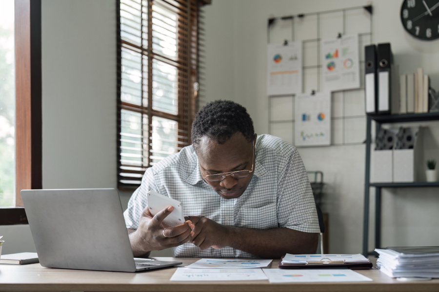 African American man calculating using machine managing household finances at home, focused biracial male make calculations on calculator account taxes or expenses