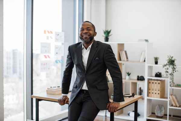 Company leader resting on edge of office desk